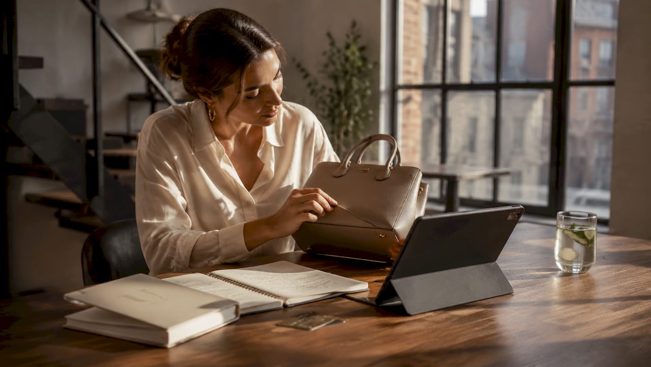 Woman checking designer fashion items on smartphone and handbag