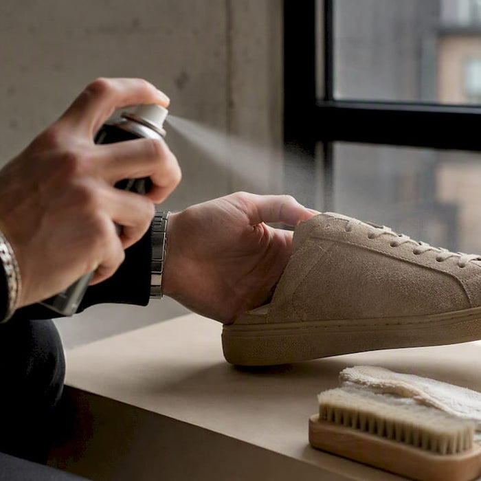 Hands spraying suede sneaker with protector