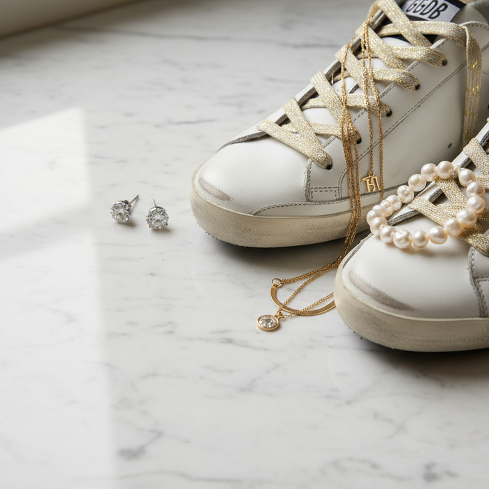 A stylish pair of Golden Goose vintage shoelaces on white sneakers, complemented by elegant jewelry such as pearls and sparkling earrings, showcasing unique styles for footwear.