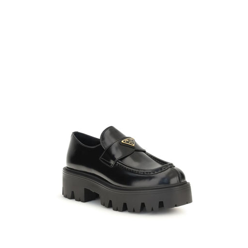 Prada Black Brushed Leather Slip-On Loafers for Women with Triangle Logo, angled front view highlighting the enameled Prada triangle logo, leather vamp strap, moc-toe stitching, and lugged rubber sole. Prada Loafers for Women from Urbalenti NYC, style 13879, SKU 79661334579, Black, Discount_30-39, available in EU36.5/US6.5, EU36/US6, EU37/US7, EU38.5/US8.5, EU39/US9, and EU40/US10; in-stock, Loafers - Shoes, New with tags, Prada, Shoes, Slip-On Loafers - Loafers - Shoes, Women.