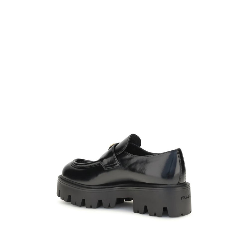 Prada Black Brushed Leather Slip-On Loafers for Women with Triangle Logo, rear-side view showing glossy calf leather, structured heel, deep lug tread, and Prada branding on the rubber sole. Prada Loafers for Women from Urbalenti NYC, style 13879, SKU 79661334579, Black, Discount_30-39, available in EU36.5/US6.5, EU36/US6, EU37/US7, EU38.5/US8.5, EU39/US9, and EU40/US10; in-stock, Loafers - Shoes, New with tags, Prada, Shoes, Slip-On Loafers - Loafers - Shoes, Women.