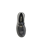Prada Black Brushed Leather Slip-On Loafers for Women with Triangle Logo, top-down view showcasing the rounded toe, stitched apron, leather vamp strap, gold-tone Prada triangle emblem, and branded insole. Prada Loafers for Women from Urbalenti NYC, style 13879, SKU 79661334579, Black, Discount_30-39, available in EU36.5/US6.5, EU36/US6, EU37/US7, EU38.5/US8.5, EU39/US9, and EU40/US10; in-stock, Loafers - Shoes, New with tags, Prada, Shoes, Slip-On Loafers - Loafers - Shoes, Women.
