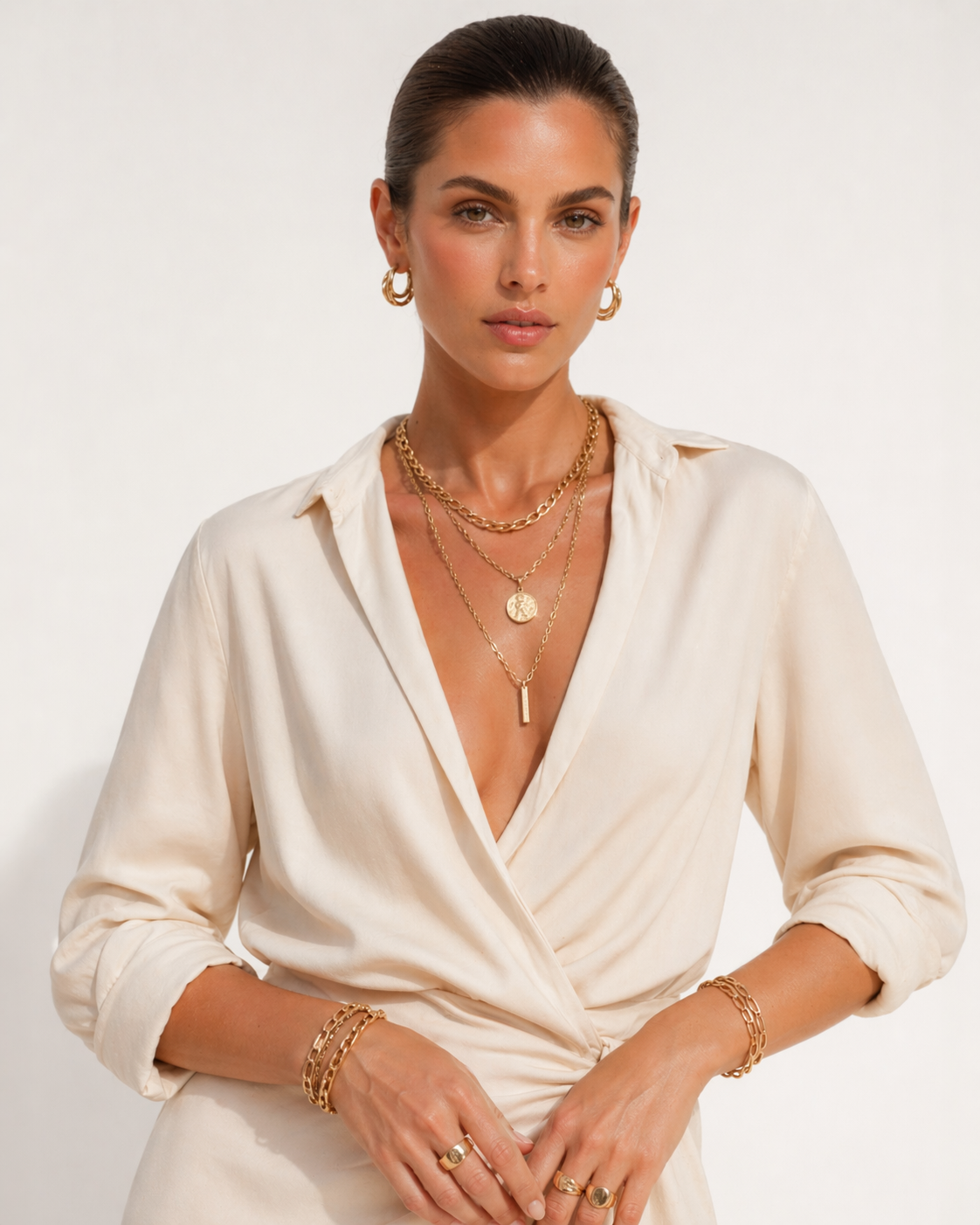 Woman wearing a white dress with gold jewelry on a plain background